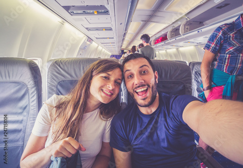 Young handsome couple taking a selfie on the airplane during flight around the world. They are a man and a woman, smiling and looking at camera. Travel, happiness and lifestyle concepts.