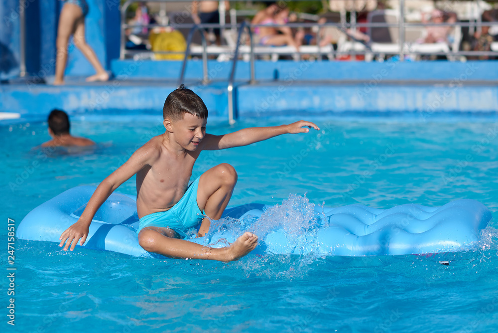 Cute European boy is using blue air mattress, while having fun in hotel’s swimming pool.