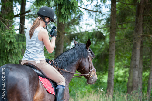 Teenage girl equestrian with smartphone riding horse taking picture
