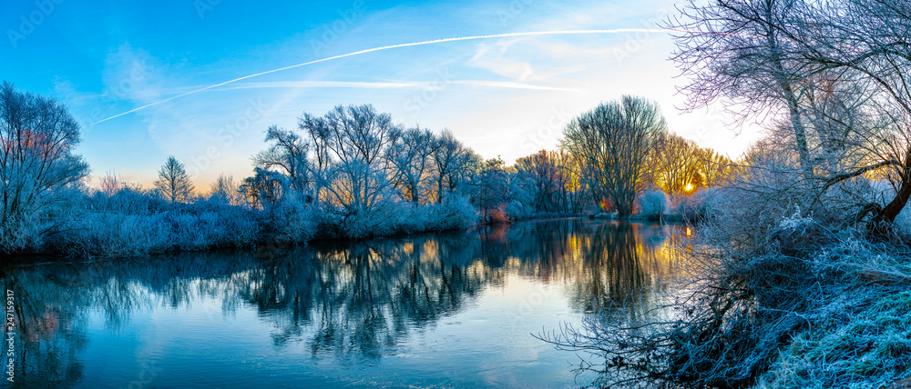 Panorama of a river in the early winter morning during colorful sunrise