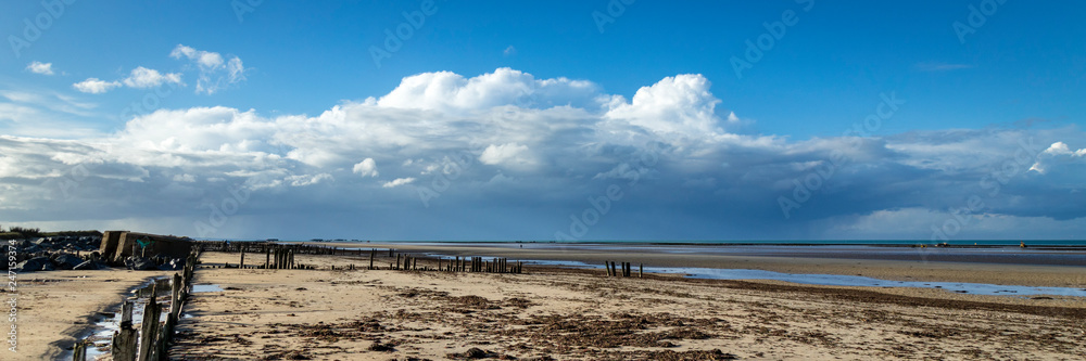 the normandy beaches in france showing ruins and relics from world war II on golden sands and dark blue waters