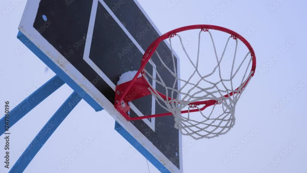 Basketball ball flies into the basket in the winter. It's snowing outside. Basketball ball flies into the basket in the winter. It's snowing outside.