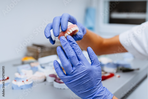 Dental prosthesis, prosthetics work. Close up of prosthetic's hands while working on the denture. Selective focus. photo