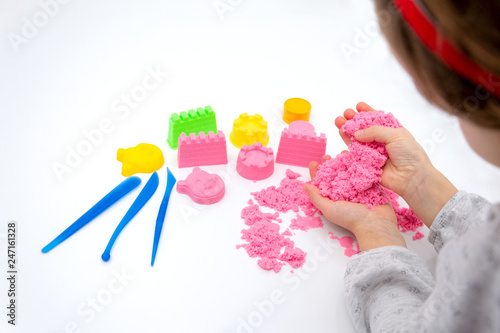 Hands of a kid playing with pink magic sand.