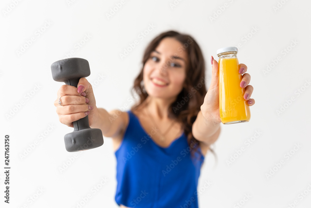 Sport, healthy lifestyle, people concept - young woman with a dumbbell in her hand and a bottle of juice in another hand Sport, healthy lifestyle, people concept - young woman with a dumbbell in her hand and a bottle of juice in another hand