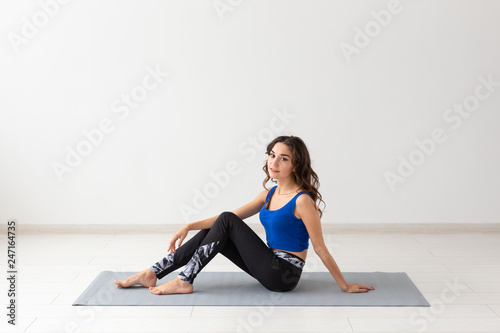 People, sport, yoga and healthcare concept - Smiling young woman sitting on exercise mat