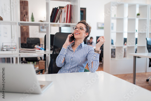 Beautiful smiling administrative assistant talking on smart phone at work.