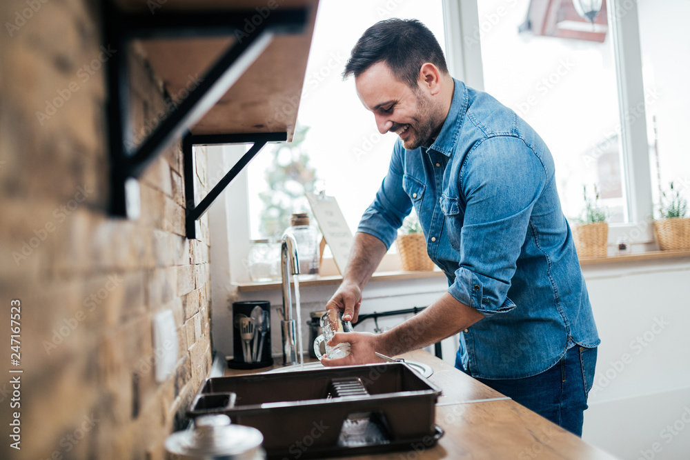 Handsome smiling man washing dishes in the kitchen, side view. Handsome smiling man washing dishes in the kitchen, side view.