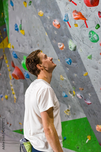 Rock climber stands and looks at the climbing wall with hooks in the boulder hall