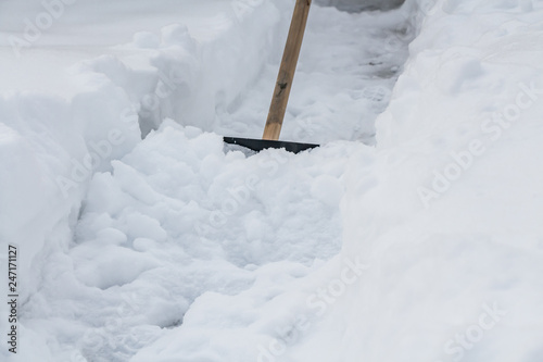 A black shovel with a yellow wooden handle is used for clean white snow from the path in winter
