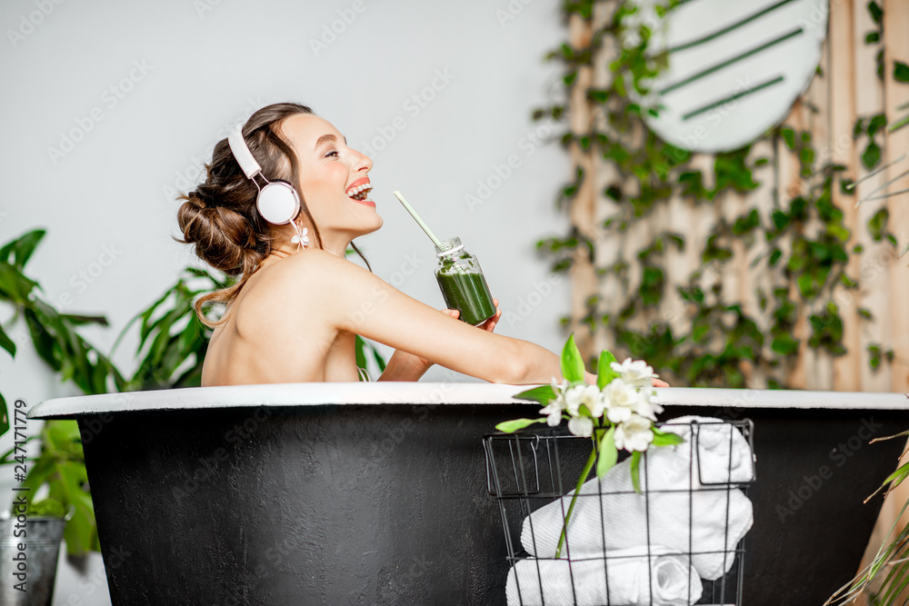 Φωτογραφία Young relaxed woman listening to the music and drinking smoothie while lying in