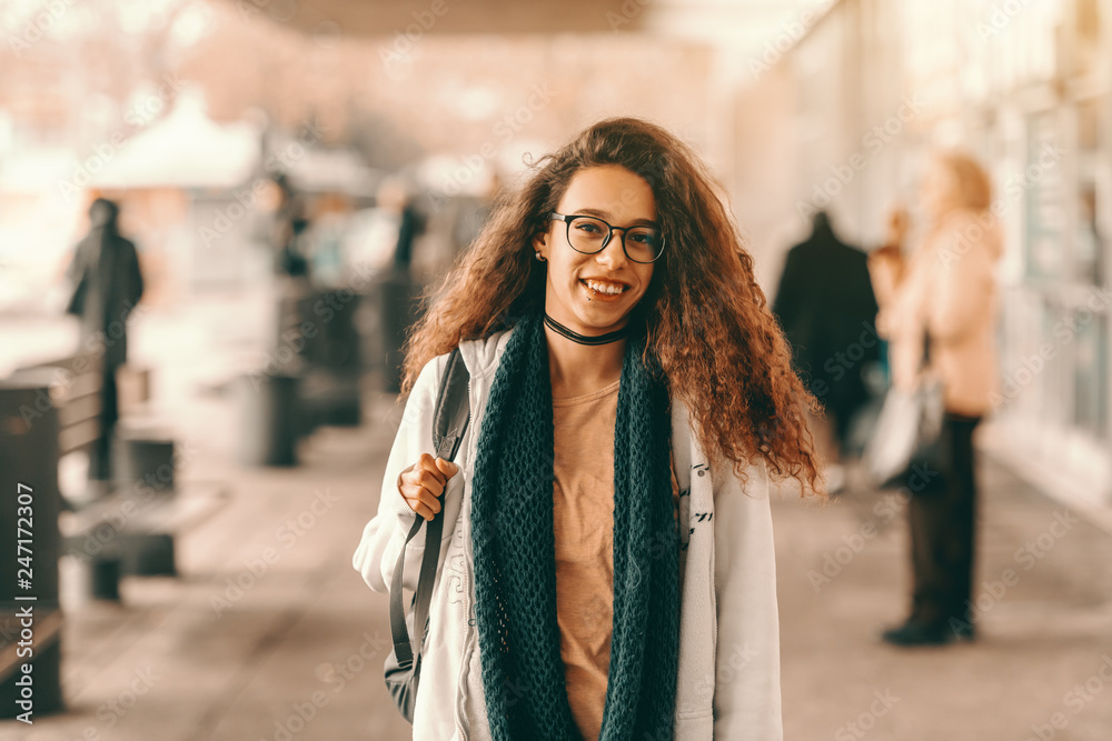 Smiling beautiful mixed race hipster girl with long curly hair stranding at the bus station in spring. Smiling beautiful mixed race hipster girl with long curly hair stranding at the bus station in spring.