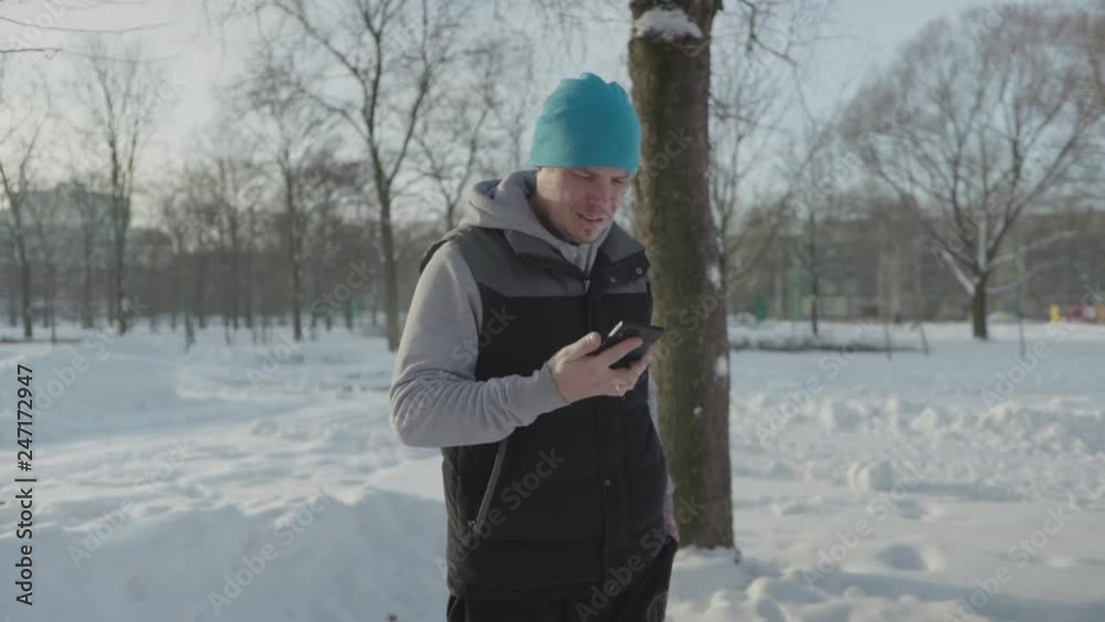 A man pulls a phone out of his pocket and talks, in the background are trees, he is wearing a jacket and vest A man pulls a phone out of his pocket and talks, in the background are trees, he is wearing a jacket and vest