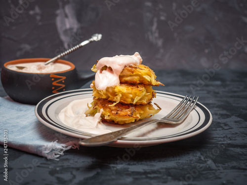 Cabbage oladi are lying on a plate on a plate, poured with sour cream, a cup of stewed sour cream on a dark wooden table, denim napkin, cutlery. photo