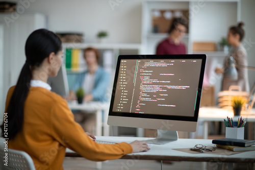 Fotografía Young female programmer in casualwear sitting by desk in front of computer scree