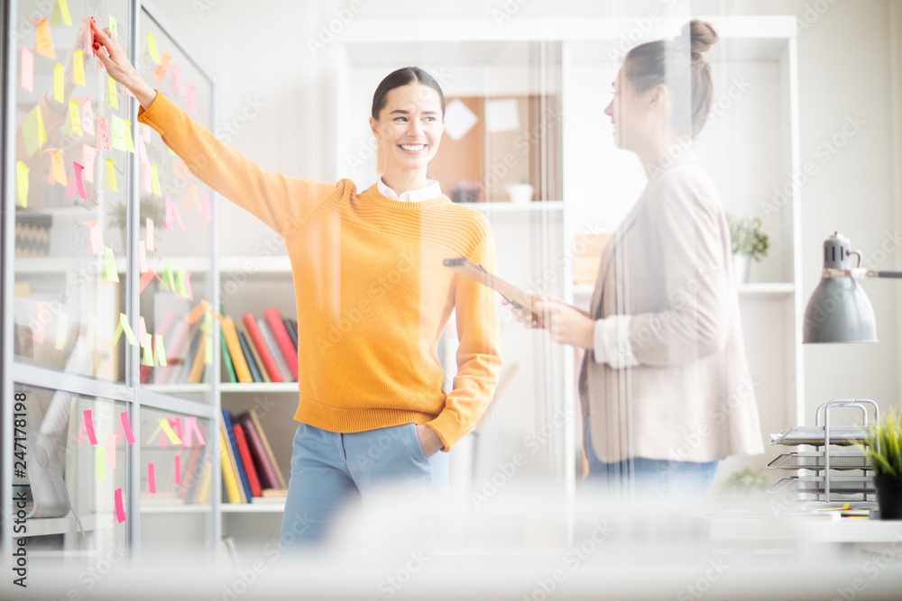 Obraz premium Two young confident females in casualwear discussing working or organization notes on noticeboard
