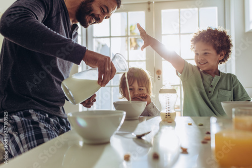 Tablou canvas Smiling father pouring milk in to bowls for breakfast