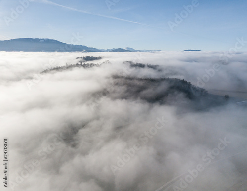 Aerial view of rural landscape in Switzerland covered with fog. Cold morning in winter with beautiful light. View from above the clouds with impressive sunlight. © Mario
