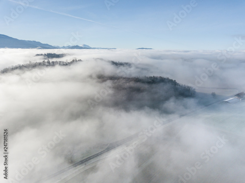 Aerial view of rural landscape in Switzerland covered with fog. Cold morning in winter with beautiful light. View from above the clouds with impressive sunlight.