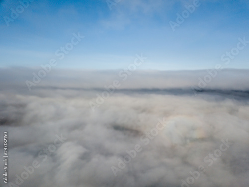 Aerial view of rural landscape in Switzerland covered with fog. Cold morning in winter with beautiful light. View from above the clouds with impressive sunlight.