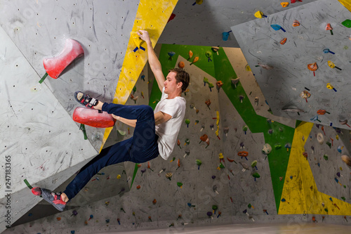 Rock climber man hanging on a bouldering climbing wall, inside on colored hooks