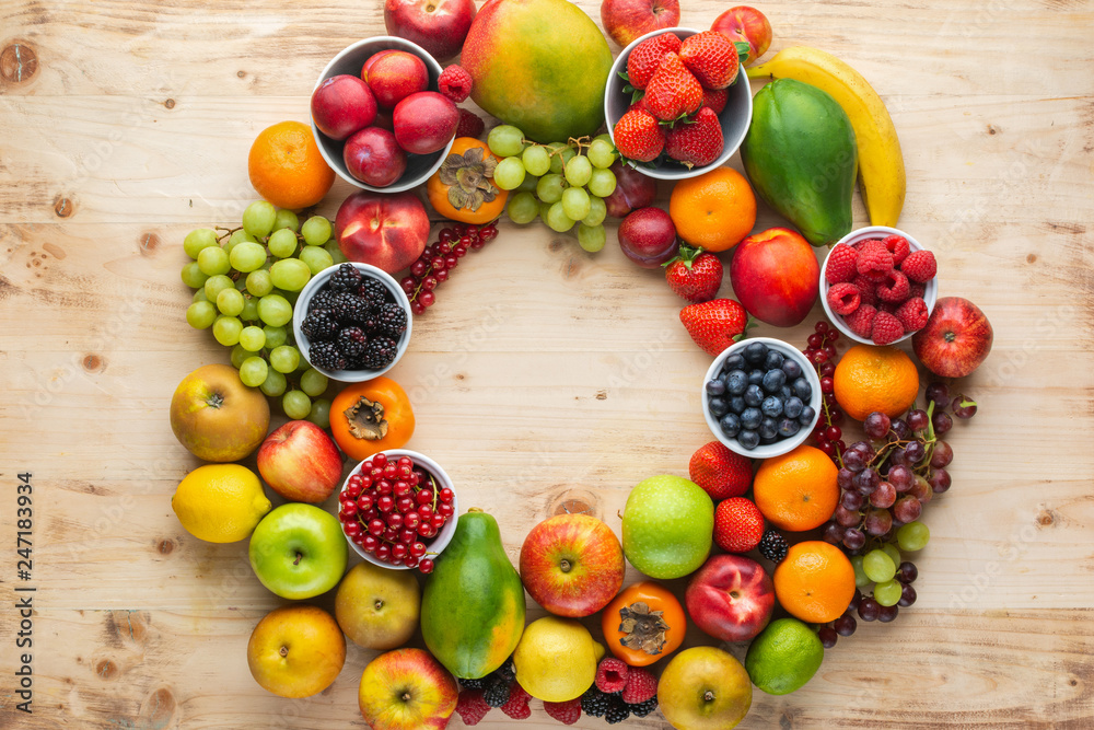 Rainbow fruits background circle frame, strawberries raspberries oranges plums apples kiwis grapes blueberries mango papaya on light wooden table, top view, copy space for text, selective focus Rainbow fruits background circle frame, strawberries raspberries oranges plums apples kiwis grapes blueberries mango papaya on light wooden table, top view, copy space for text, selective focus