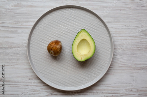 Half avocado with bone on plate over white wooden background, top view. Overhead, from above, flat lay.