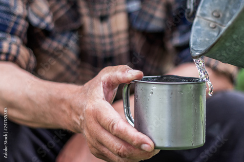 Man is holding a steel mug and a well  water is pouring from a bucket, life and thirst concept