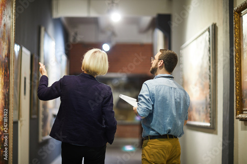 Back view portrait of two museum workers discussing paintings walking in art gallery, copy space photo