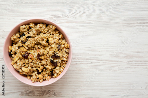 Fruit granola in pink bowl over white wooden table, top view. Flat lay, from above, overhead. Copy space.