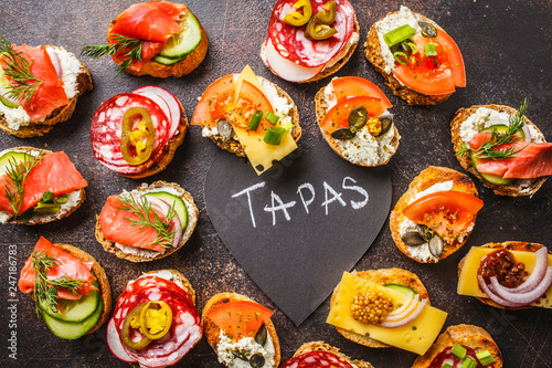 Assorted spanish tapas with fish, sausage, cheese and vegetables. Dark background, top view.