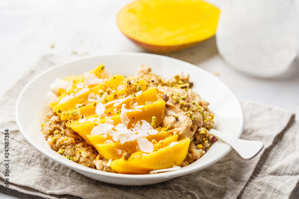 Oatmeal with mango, coconut, peanut butter and nuts in a white plate. Vegan food, healthy breakfast, plant based concept. Oatmeal with mango, coconut, peanut butter and nuts in a white plate. Vegan food, healthy breakfast, plant based concept.