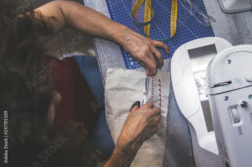 View from above middle-aged lady works in her sewing space young brunette woman sews with sewing machine creates accessories repairs mend clothes embroider and packs trendy dress. View from top