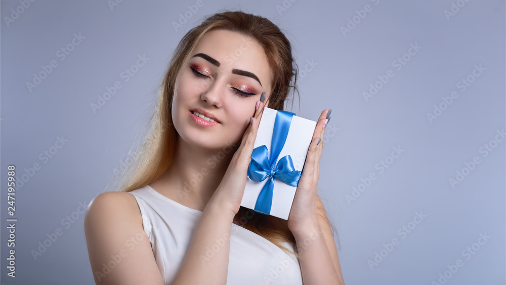 portrait of a happy woman with a gift box near the face on a studio background, the girl closed her eyes from pleasure and pressed a present with bow to her cheek, concept holidays and love and care portrait of a happy woman with a gift box near the face on a studio background, the girl closed her eyes from pleasure and pressed a present with bow to her cheek, concept holidays and love and care