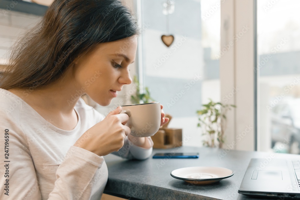 Closeup of young beautiful woman in profile with cup of fresh coffee in coffee shop Closeup of young beautiful woman in profile with cup of fresh coffee in coffee shop