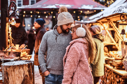 A happy attractive couple in love, enjoying spending time together while embracing at the winter fair at a Christmas time © Fxquadro