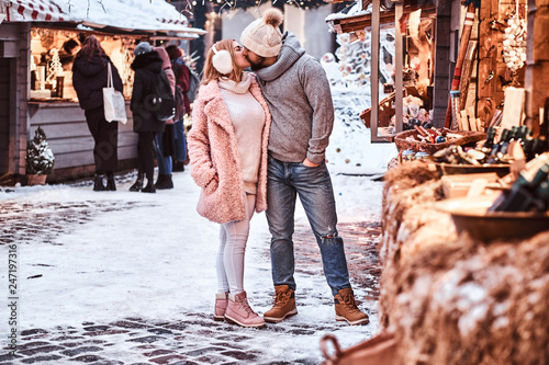 An attractive couple in love, cuddling together and kissing at the winter fair at a Christmas time.