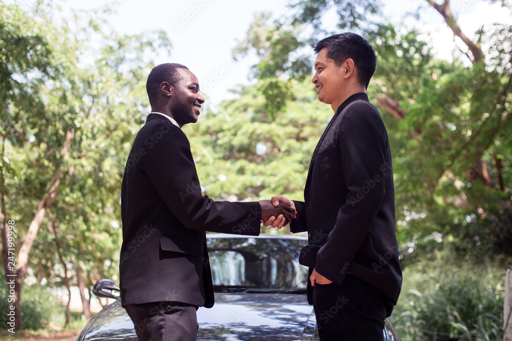 African business man and Asian business man shaking hands after meeting with green natural background. African business man and Asian business man shaking hands after meeting with green natural background.