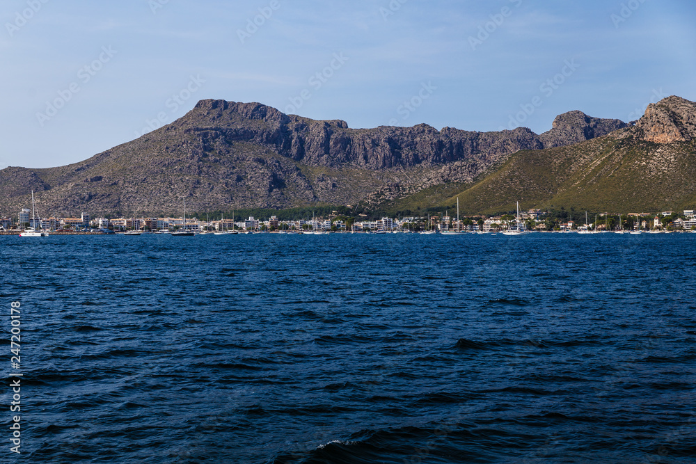 wide, blue sea waters on a sunny day, mountainous and shoreline in the distance; blue sky without clouds