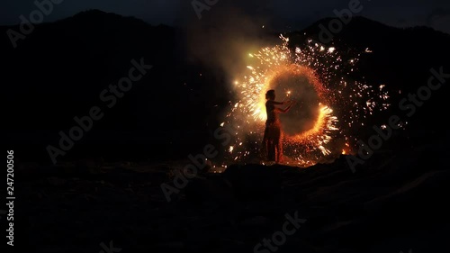 Scenery juggling with sparkling flame. Art event, presentation traveling summer season. Beautiful model standing on the improvised stage at beachline and enjoyment turning flashing sparkles torches photo
