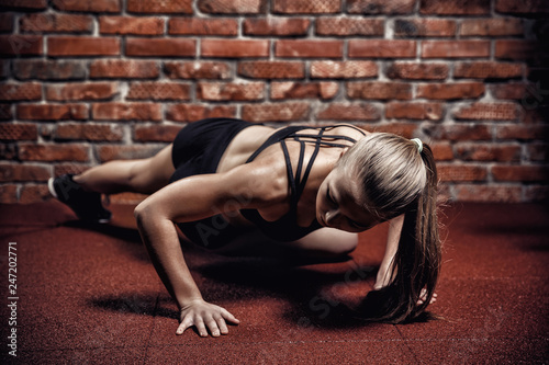 Beautiful athletic girl with press is practicing fitness on background of brick wall