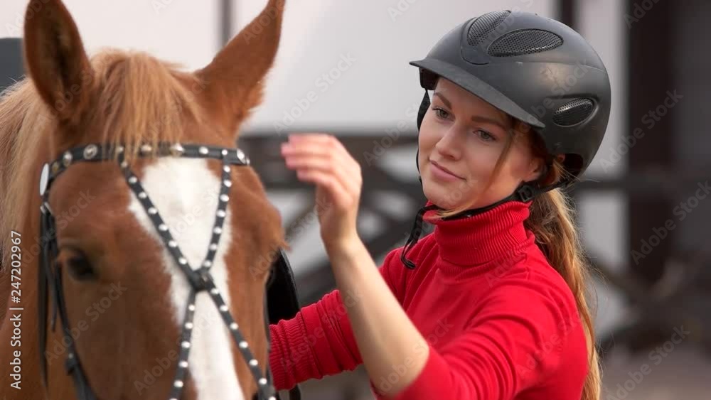Beautiful girl in helmet stroking a horse outdoors. Pretty young woman caressing a horse at the horse farm. Love between people and animals. Beautiful girl in helmet stroking a horse outdoors. Pretty young woman caressing a horse at the horse farm. Love between people and animals.
