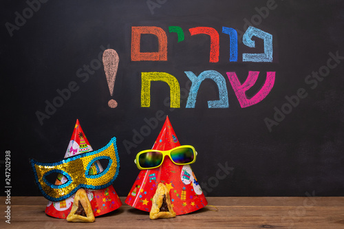 Hebrew inscription "Happy Purim" on chalkboard. Carnival caps and funny masks.