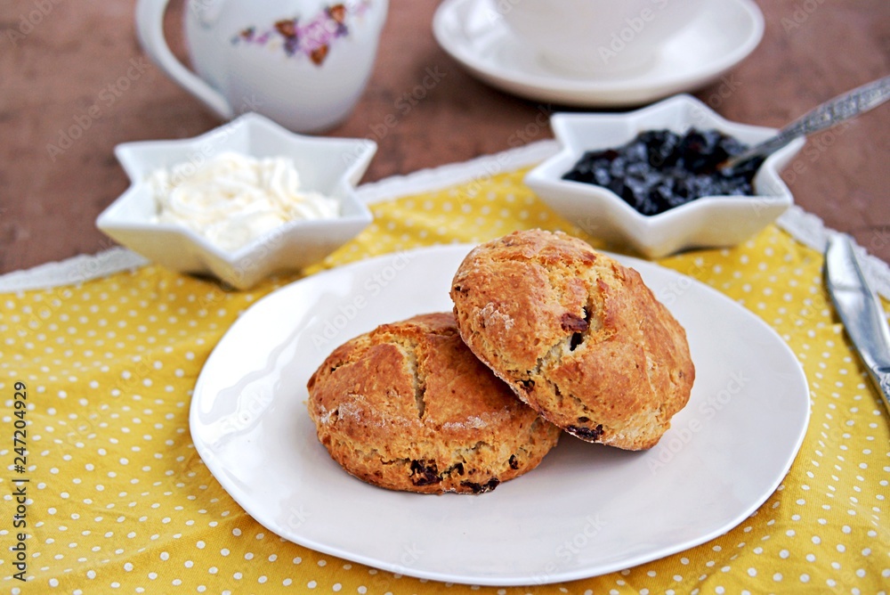 Traditional English scones with dried cranberries on a white plate. Served with jam and whipped cream.
