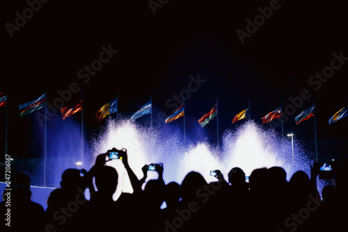 People shoots fountain and flags on smartphones. People silhouettes. Night