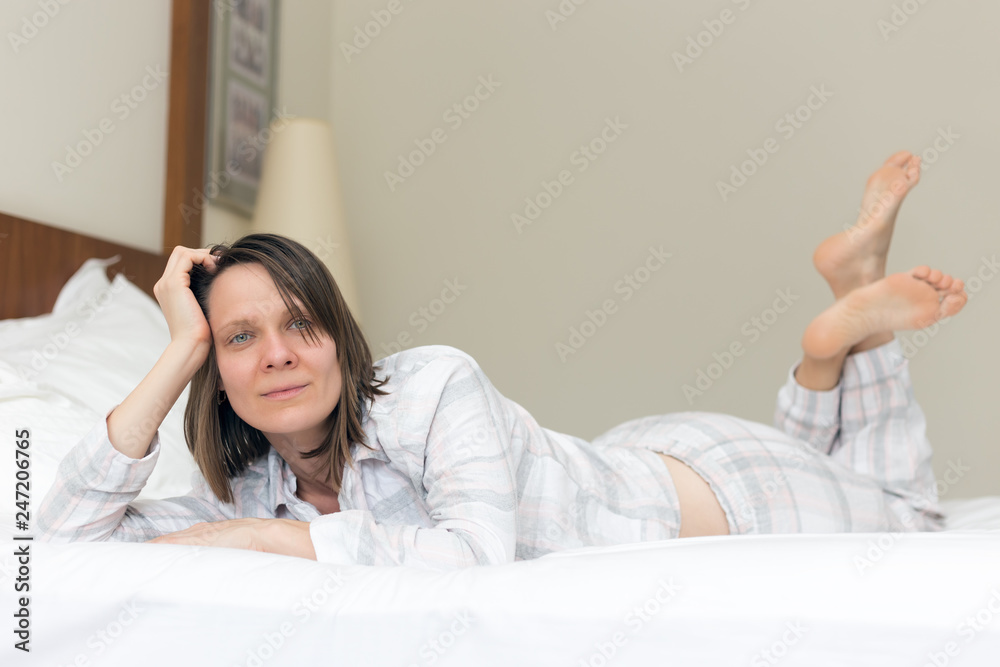 Woman with beautiful eyes and broad smile lying on bed in bedroom wearing pyjamas Woman with beautiful eyes and broad smile lying on bed in bedroom wearing pyjamas