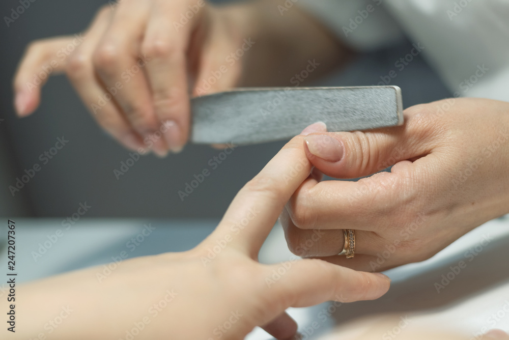 Manicurist polishes fingernails with manicure file. Nail preparation for nail polish.