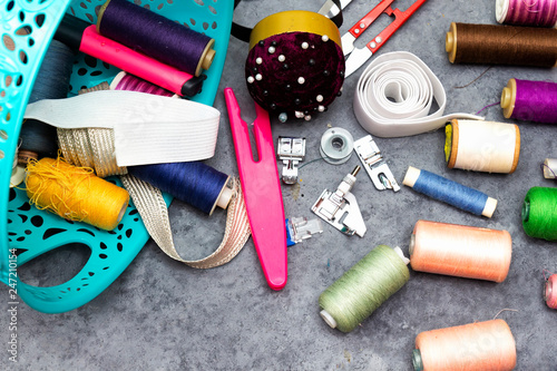 basket of sewing tools :  scissors, colorful  bobbins with thread and presser foot on gray  wooden table