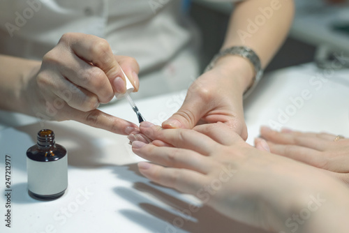 Manicurist is applying a nail base gel on a female finger nails. Nail care concept.