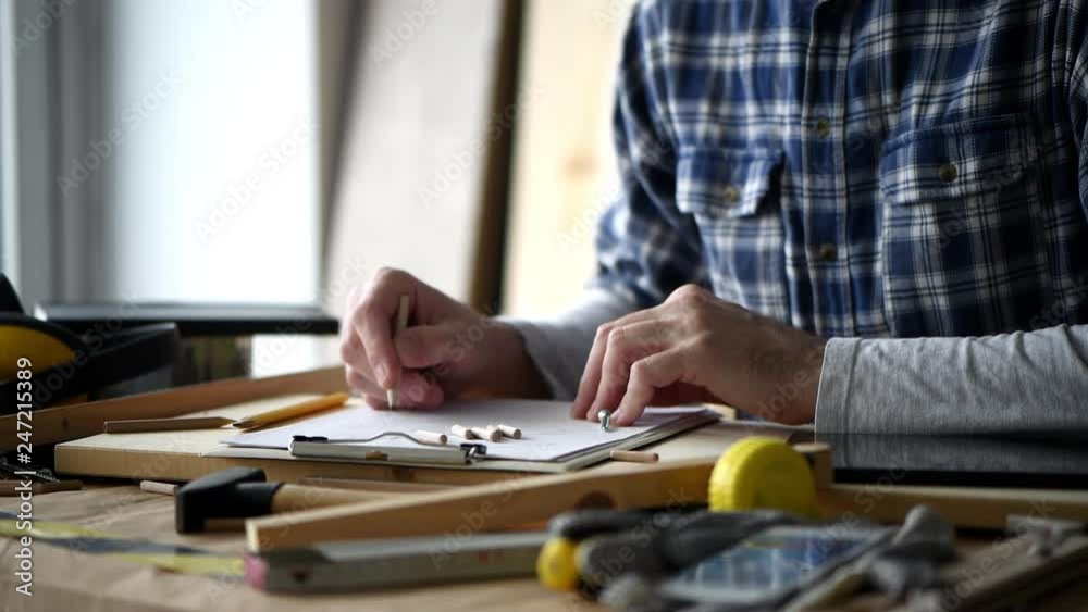 Carpenter sketching woodwork project on clipboard paper in his small business workshop Carpenter sketching woodwork project on clipboard paper in his small business workshop
